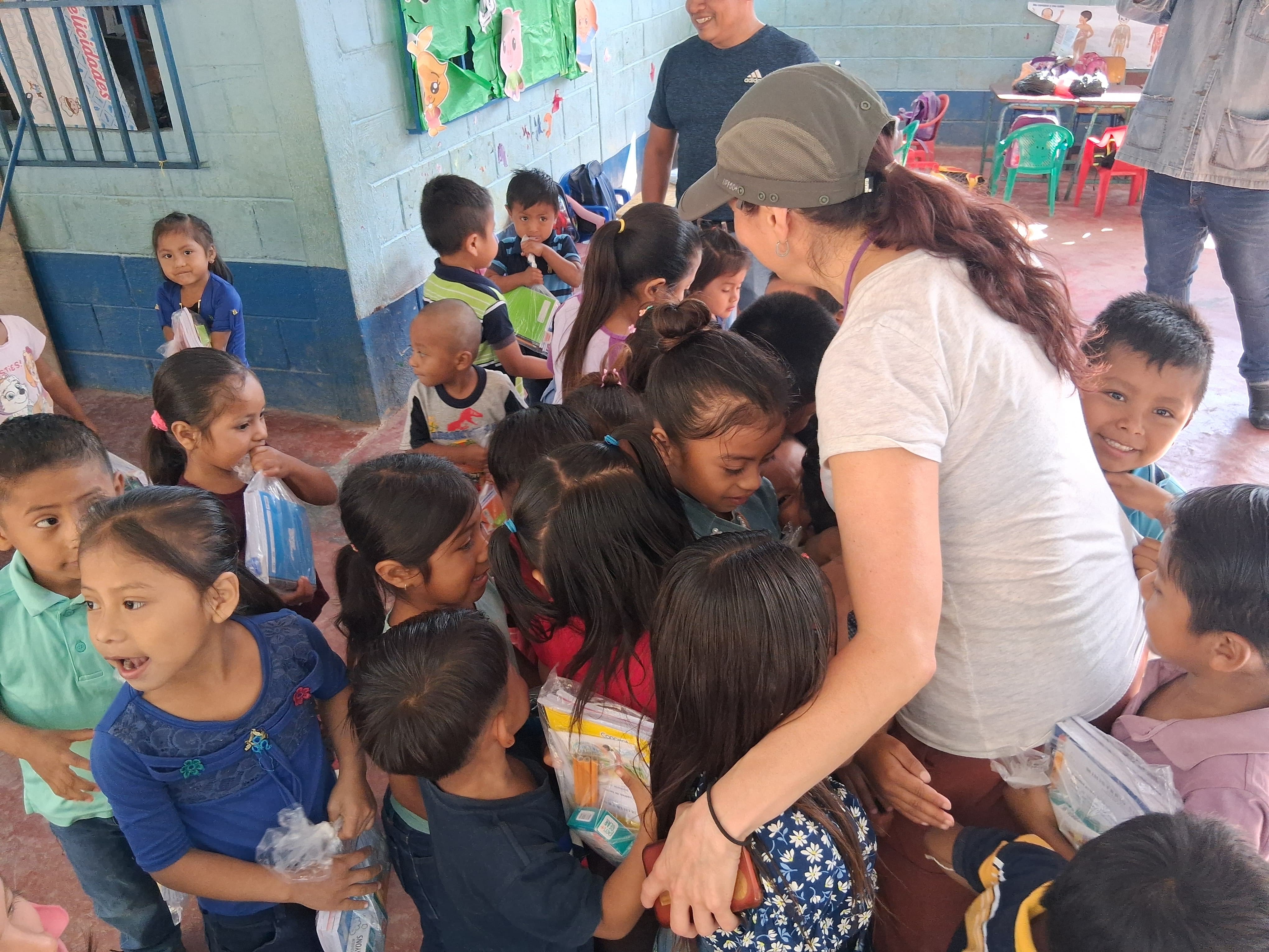A volunteer handing out school supply kits to a group of children inside a classroom