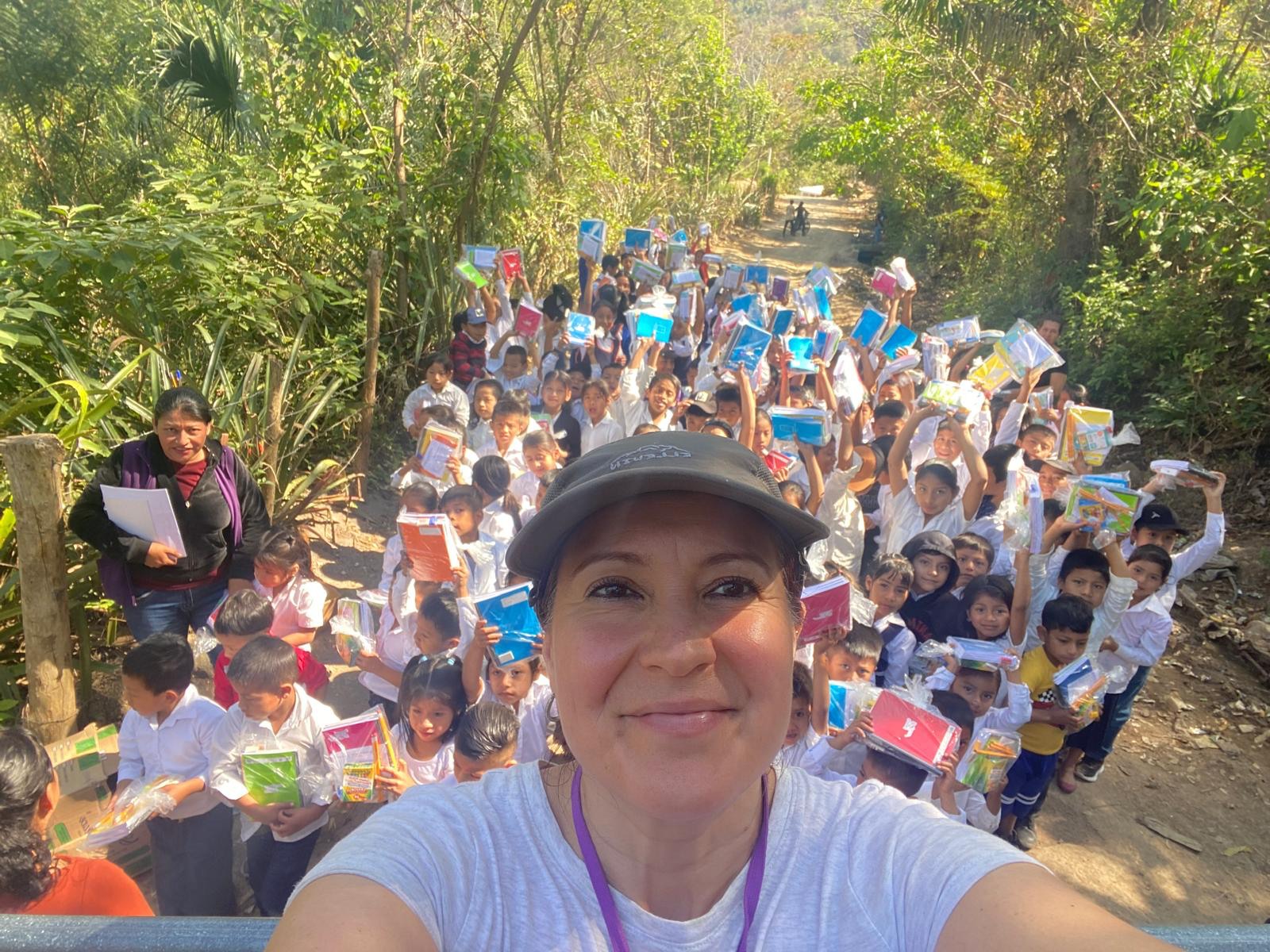 A volunteer with a long line of schoolchildren holding up donated school supplies along a countryside trail
